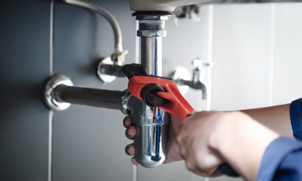 Plumber uses wrench to repair water pipe under sink There is maintenance to fix the water leak in the bathroom.with red wrench, plumbing install concept.